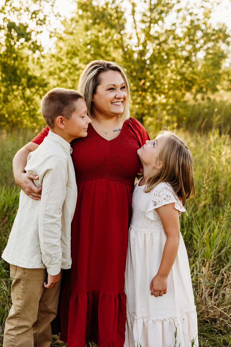 mom in red dress hugging her two kids wearing white clothing