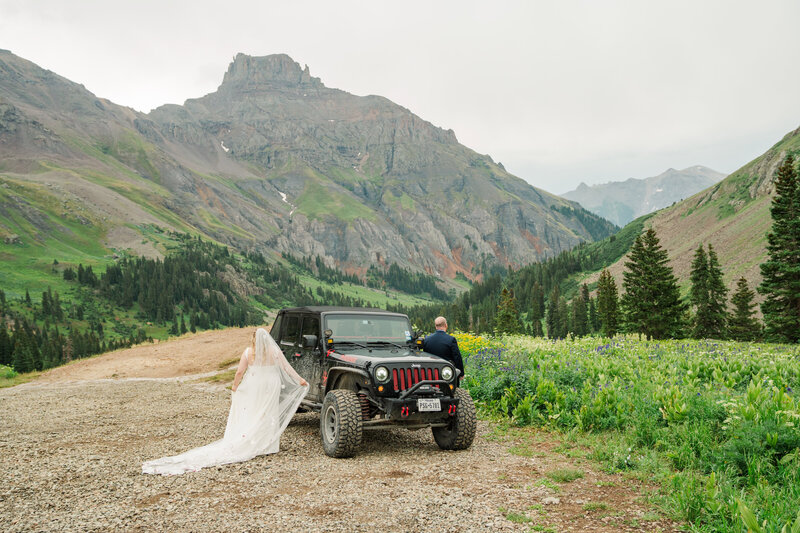 A couple stands with their two small children and officiant next to a lake and mountains