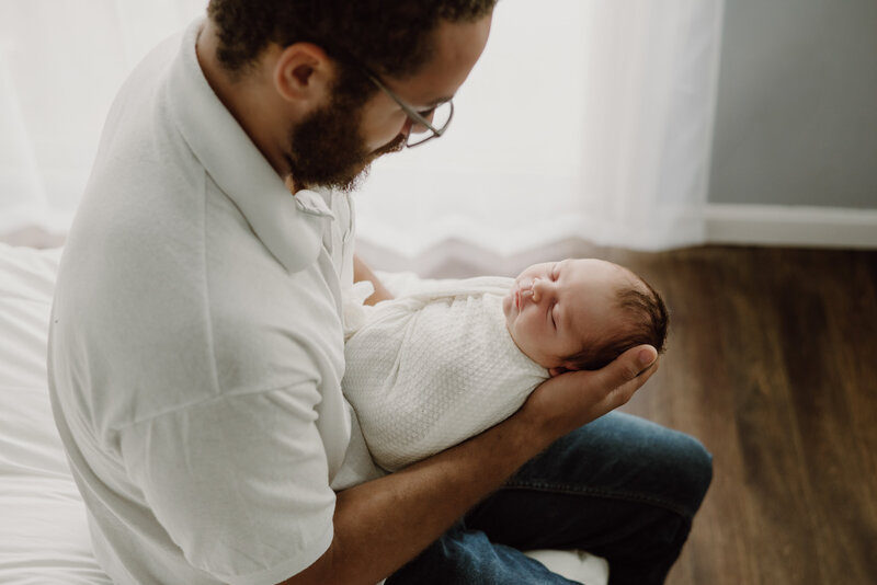 Newborn photo of dad holding baby boy wrapped in white blanket in studio in Annapolis Maryland.
