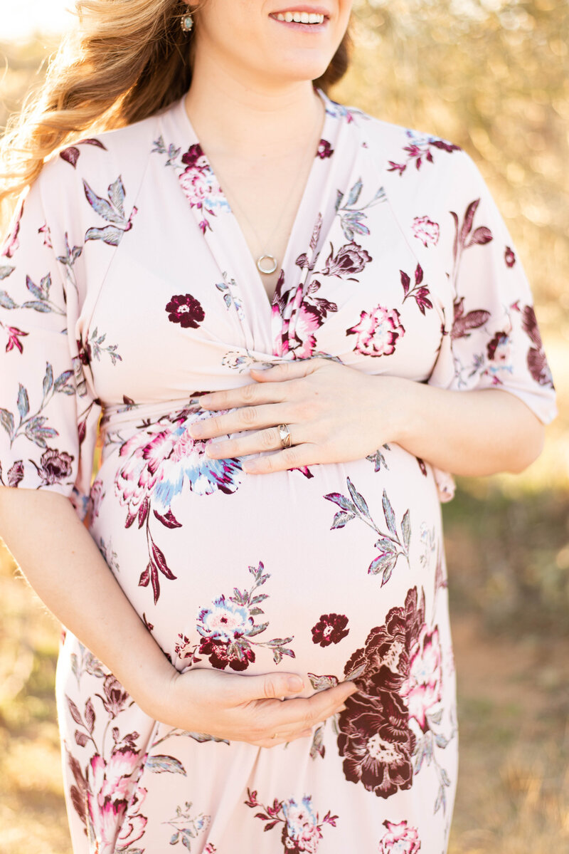 Mother wearing a flower dress, holding her baby bump.