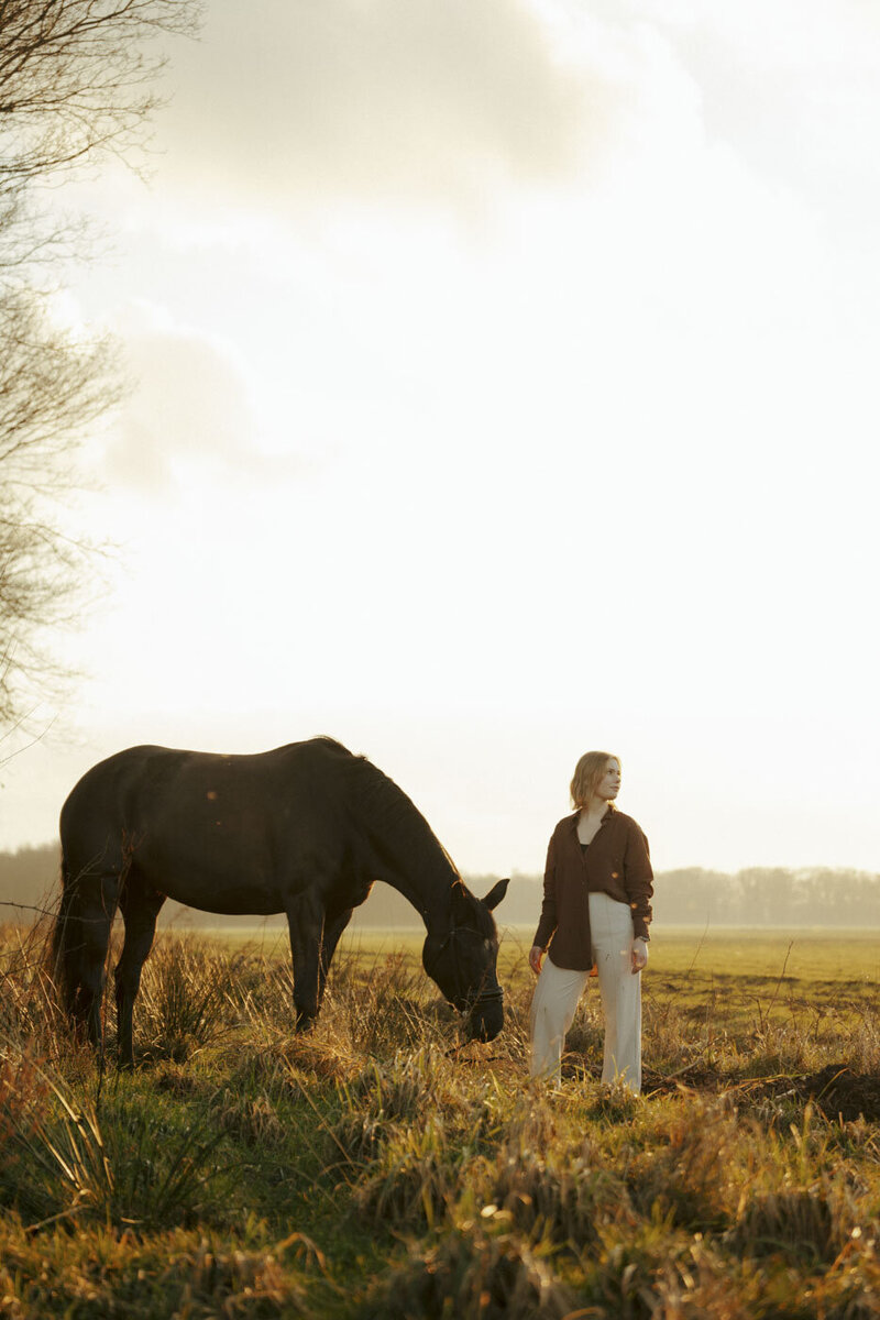 Filmische fotoshoot bij zonsondergang met vrouw en paard in natuurlijke setting, vastgelegd door verhalend fotograaf Alina Nieman.
