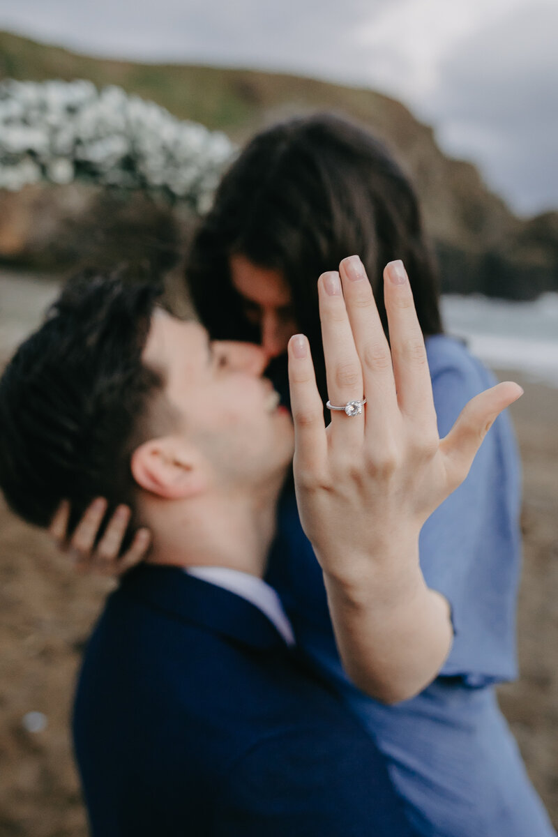 Engagement photoshoot on a Waterford beach, with the groom-to-be lifting his fiancée in his arms as she proudly shows off her ring to the camera