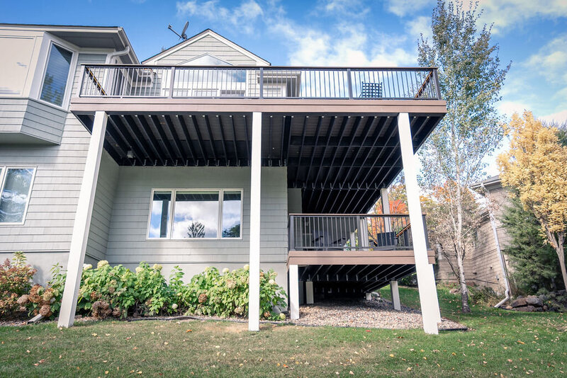 Back of a house with a large upper deck and small lower deck, both with white wrapped posts supporting them. 