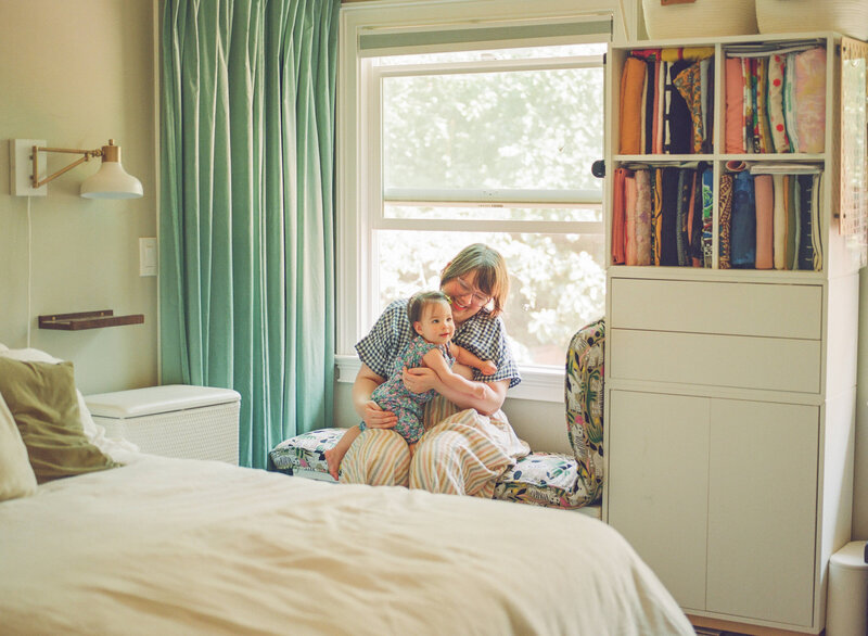 mom sitting in window seat holding baby daughter while both smiles