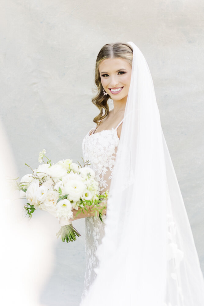 bride smiling in wedding dress with veil flowing by her side