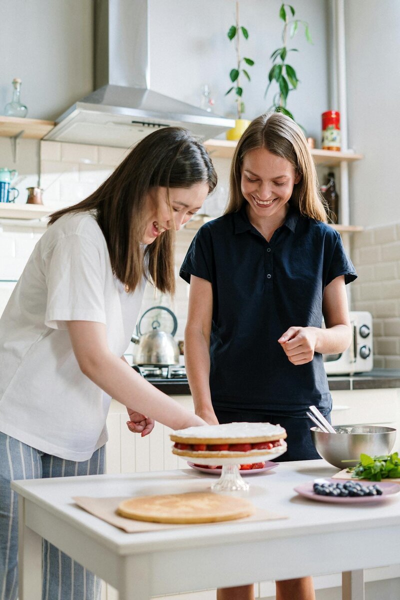 Two women smiling and preparing food together in a kitchen representing connection and collaboration during the first intake session at Rooted & Nourished Psychotherapy