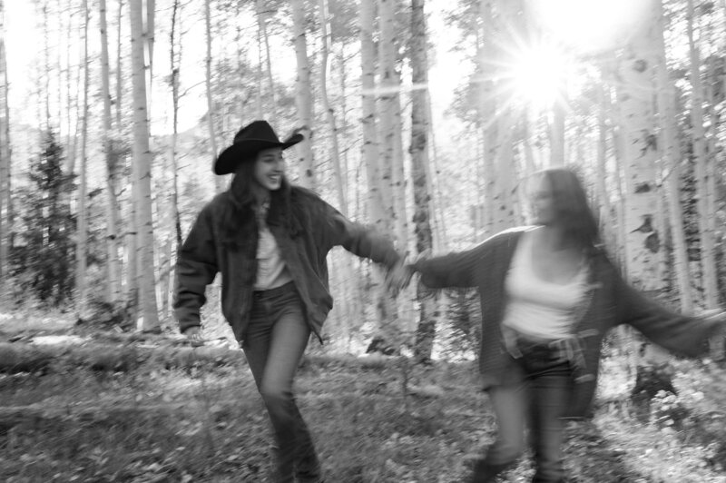 two women holding hands running in forest