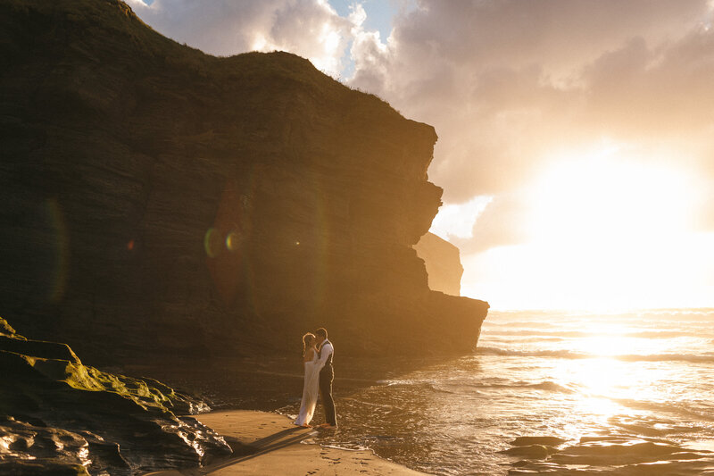 Couple at sunset on the beach with story seas and high cliffs in view