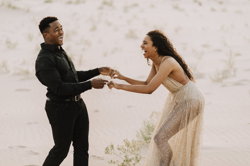 couple laughing holding hands in sand dunes