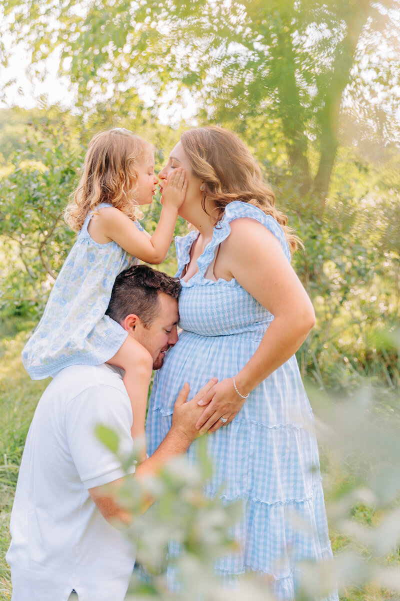 Asheville Maternity Photographer captures family photos with toddler daughter and dad giving kisses and snuggles with Rachel Marie Photography