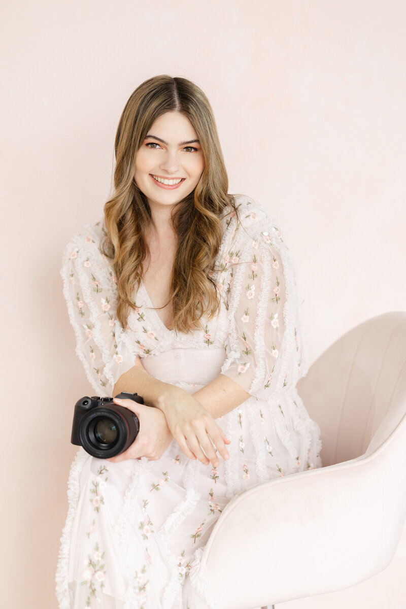 New England Wedding Photographer Liana Huot is captured standing behind a wedding tablescape. She is smiling at the camera with her own camera in hand.