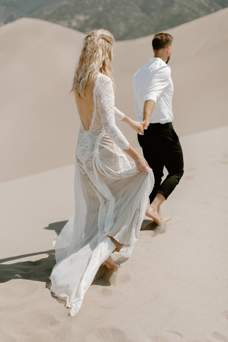 man and woman walking on sand dune