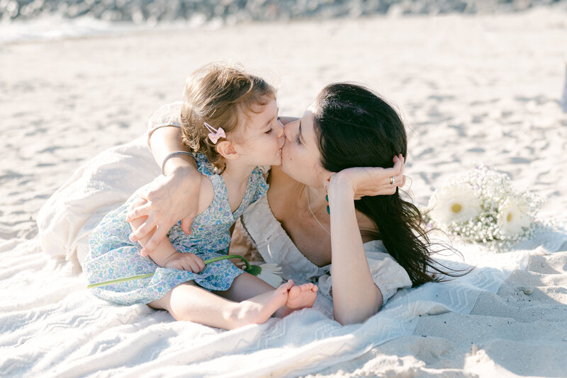 Mom kissing her daughter on the beach