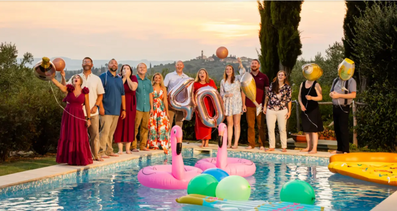 Friends and family gathered poolside holding “40” balloons at sunset during a milestone birthday celebration in the Tuscan hills.
