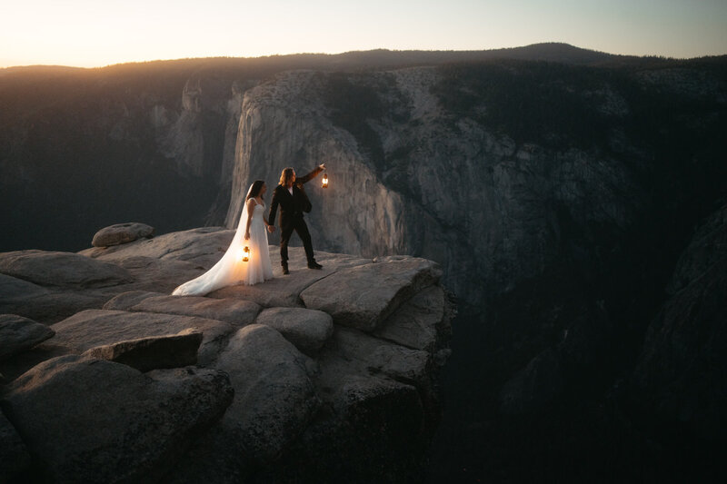 Couple stands on the edge of a cliff with lanterns at Taft Point, the best Yosemite Elopement Location