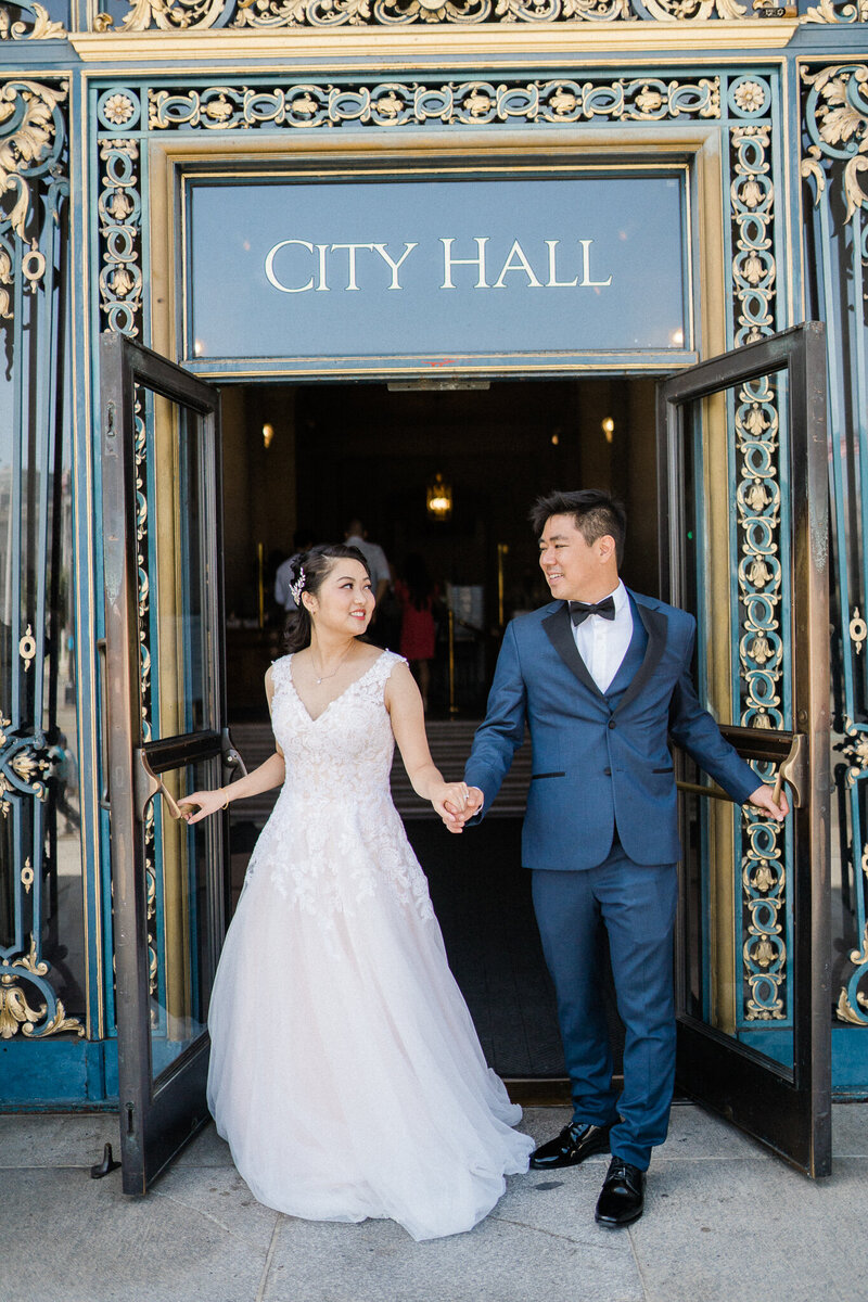 husband and wife walk outside san francisco city hall after marriage ceremony