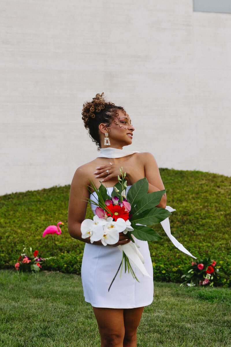A bride posing her a bouquet outside in a white dress