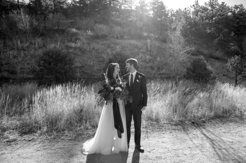 Bride and Groom stand next to each other and gaze at each other in front of tall grass.