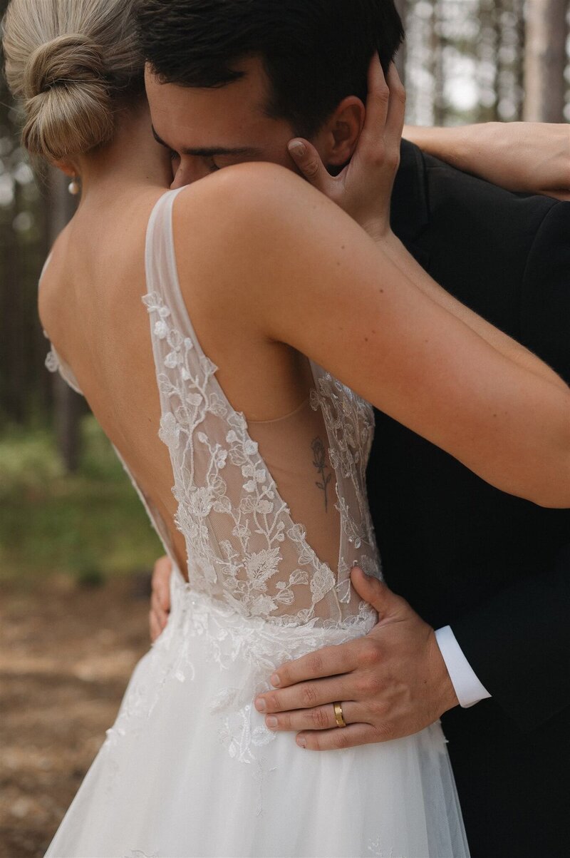 Groom kisses bride's neck as she holds his head and he holds her hips in loving embrace.