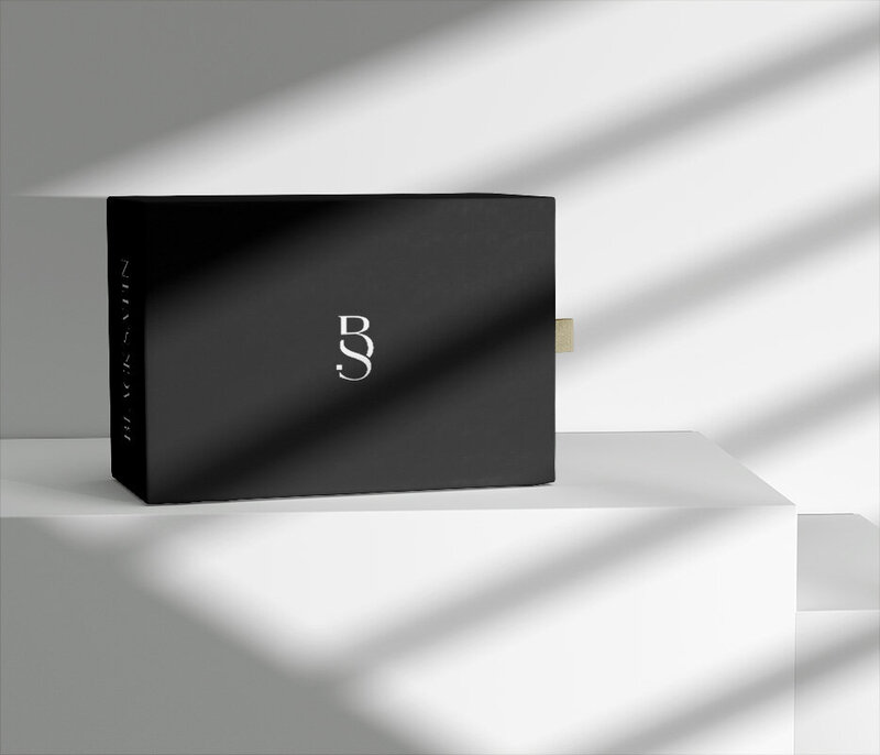 Black product box with logo, on a white surface, with diagonal light and shadow play.