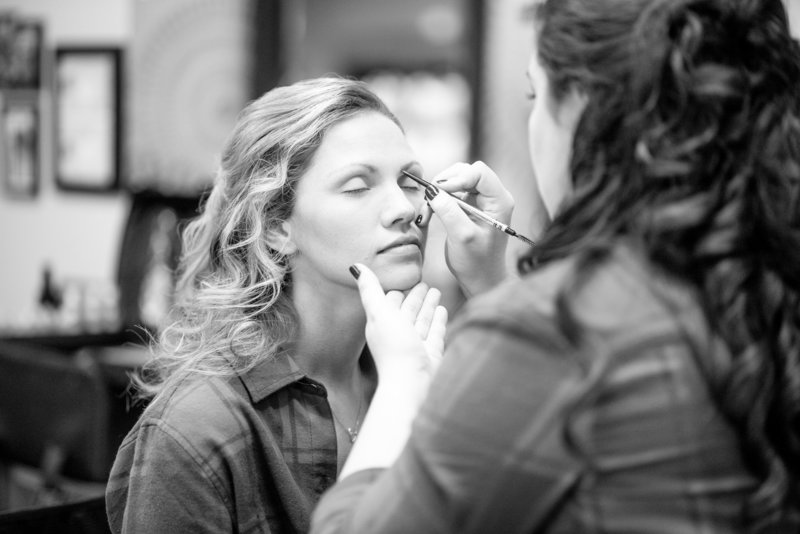 Black and white photo of a girl getting her make-up done before a wedding.