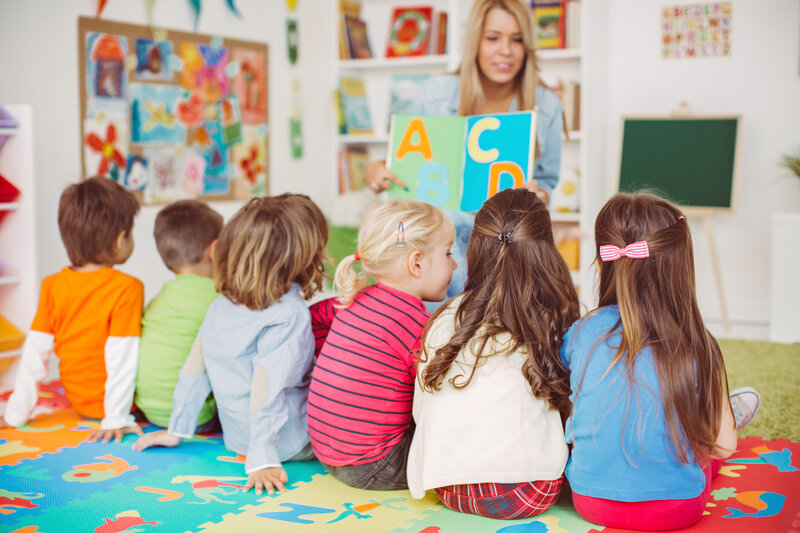 Female teacher teaching ABC's to a young group of children sitting on the floor