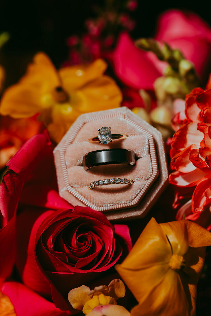 wedding bands within pink ring box  positioned on colorful flowers