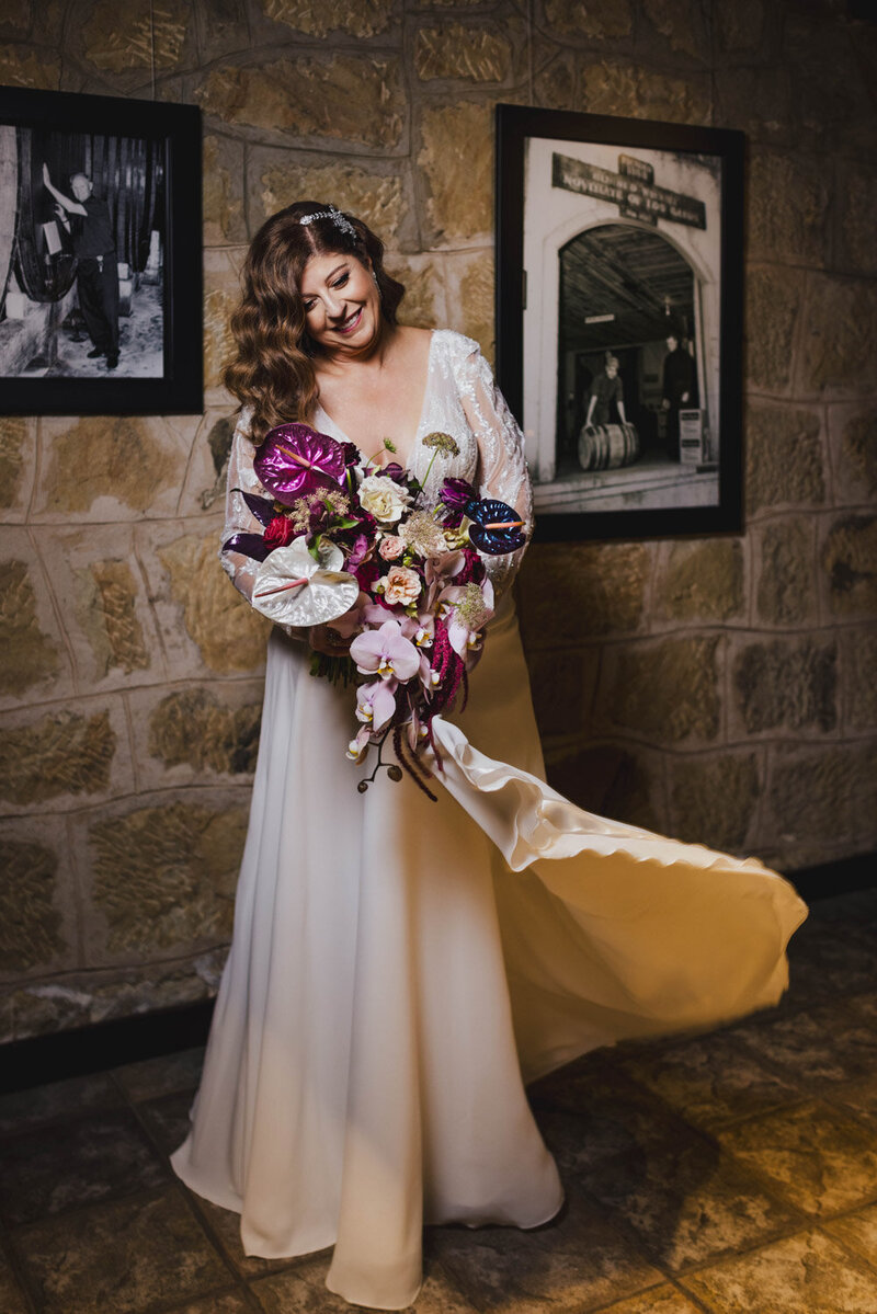 bride holding bouquet with purple tones in front of stone wall