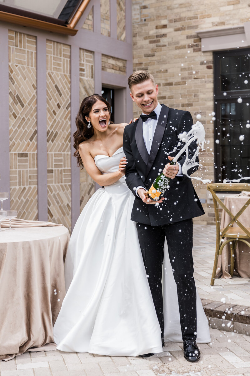 Bride and groom popping a bottle of champagne
