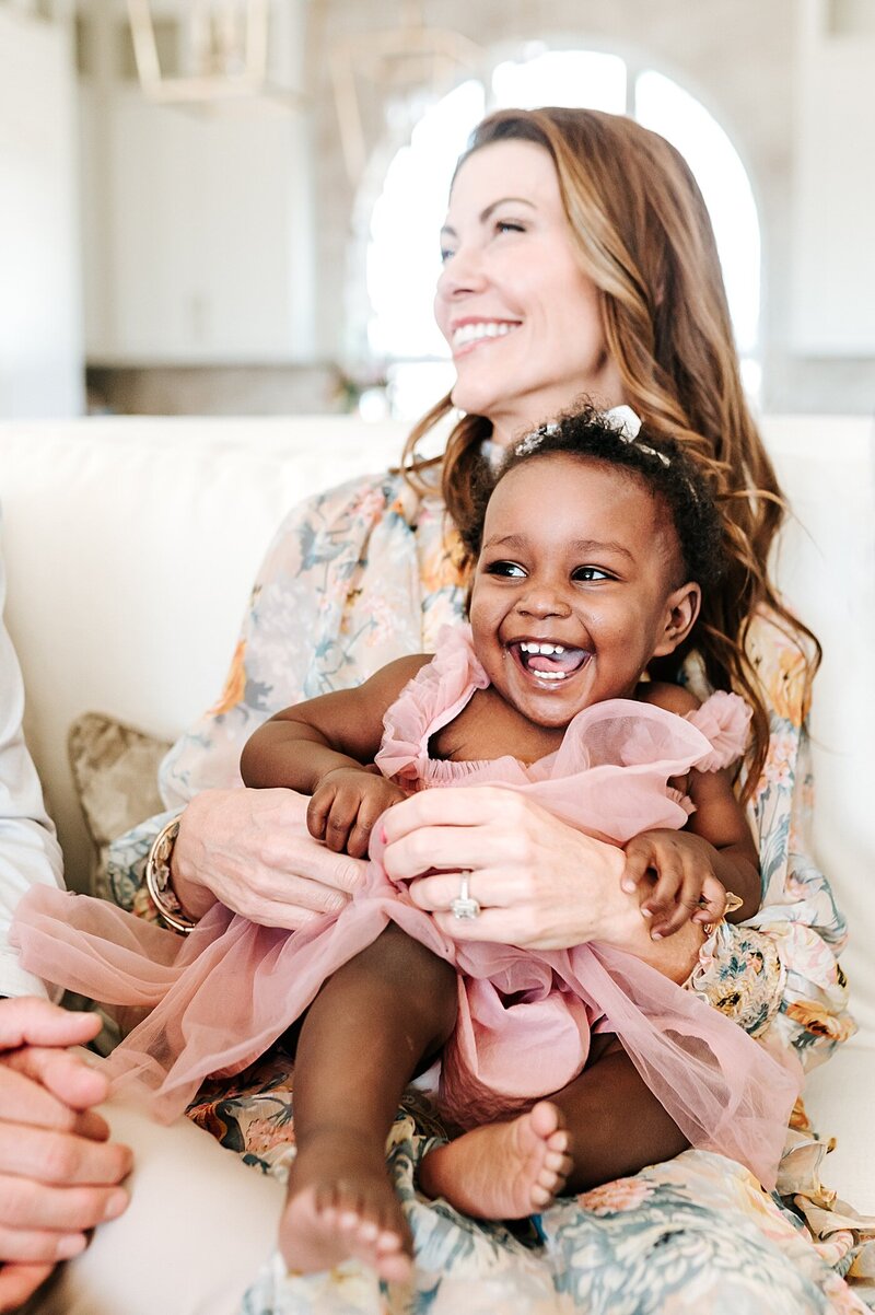 mother holding adopted daughter at home laughing