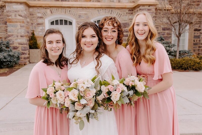 bride with her bridesmaids holding light pink rose bouquets outside the Logan LDS temple