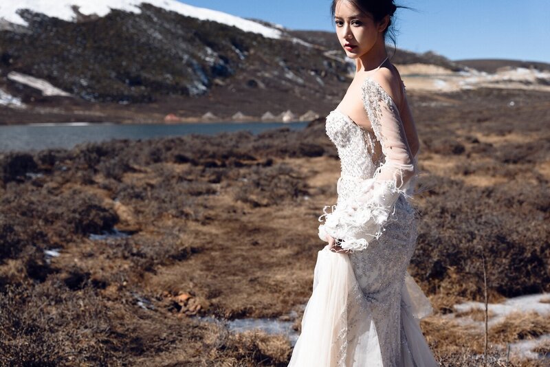 Dramatic shoot of a bride in a haute couture dress by an alpine lake in snow capped mountains.