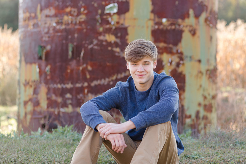 waynedale high school senior guy wearing blue long sleeve shirt, with tan pants, sitting in front of an old rusty water tank, photographed in Wooster Ohio, photographed by Jamie Lynette Photography Canton Ohio Senior Photographer