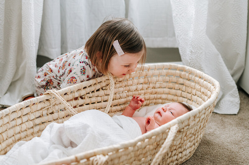 big sister & newborn baby in moses basket
