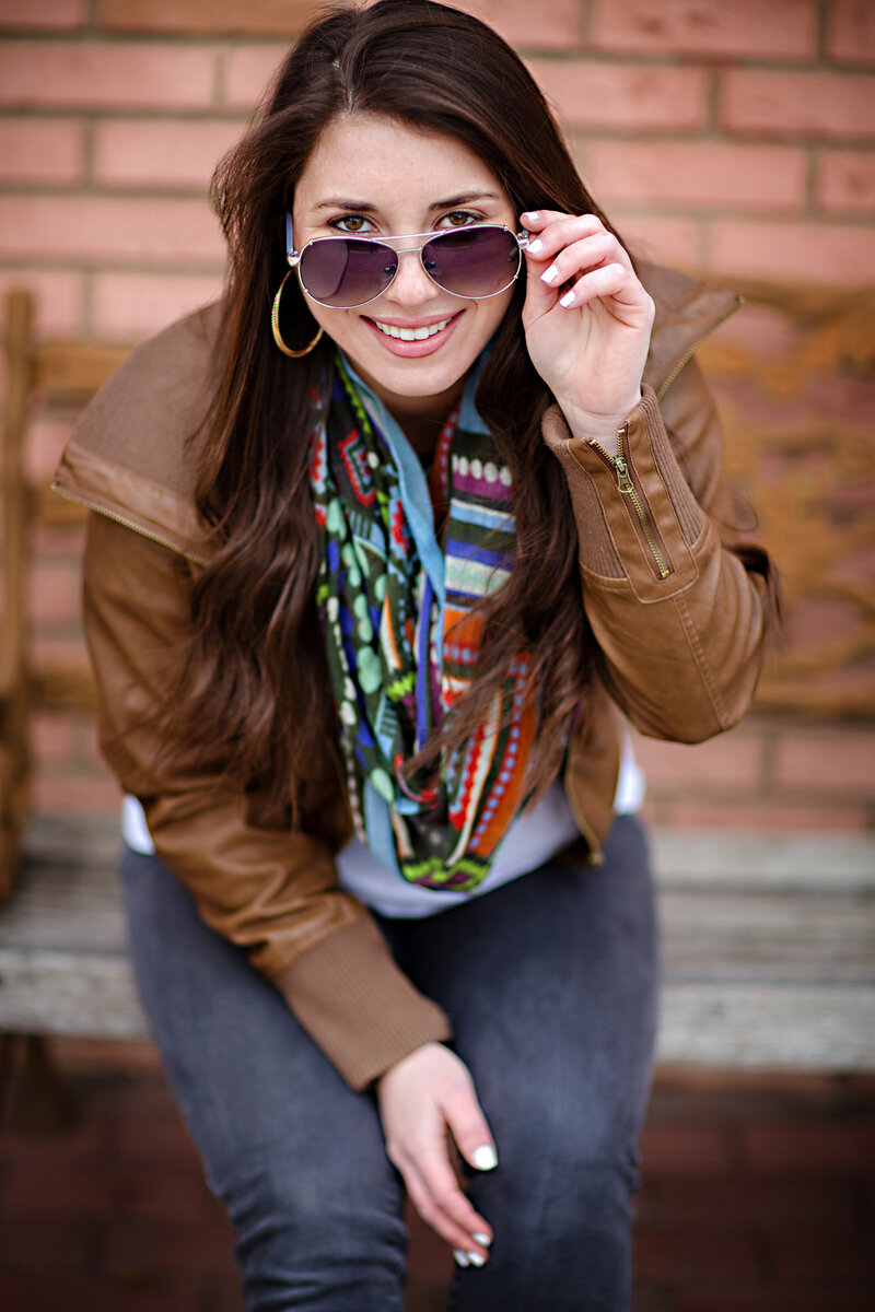 Engaging Charlotte HS Senior Pictures sitting on a bench looking at camera peeking through sunglasses