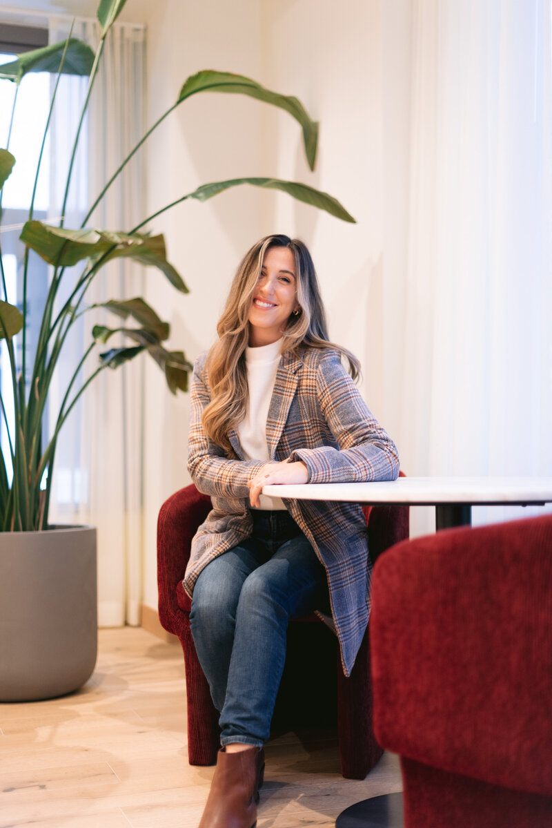Therapist with a white shirt and jeans sitting on a cream coach with a notepad and pen in hand