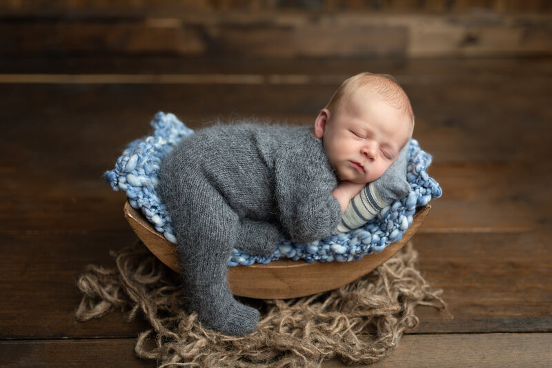 Peacefully posed in a wooden bowl with soft blue knits, this newborn boy is dressed in a fuzzy grey sleeper – a cozy rustic setup in our Paris, Ontario studio.