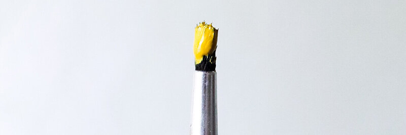 Still life photo of paintbrush standing up with yellow paint on the tip