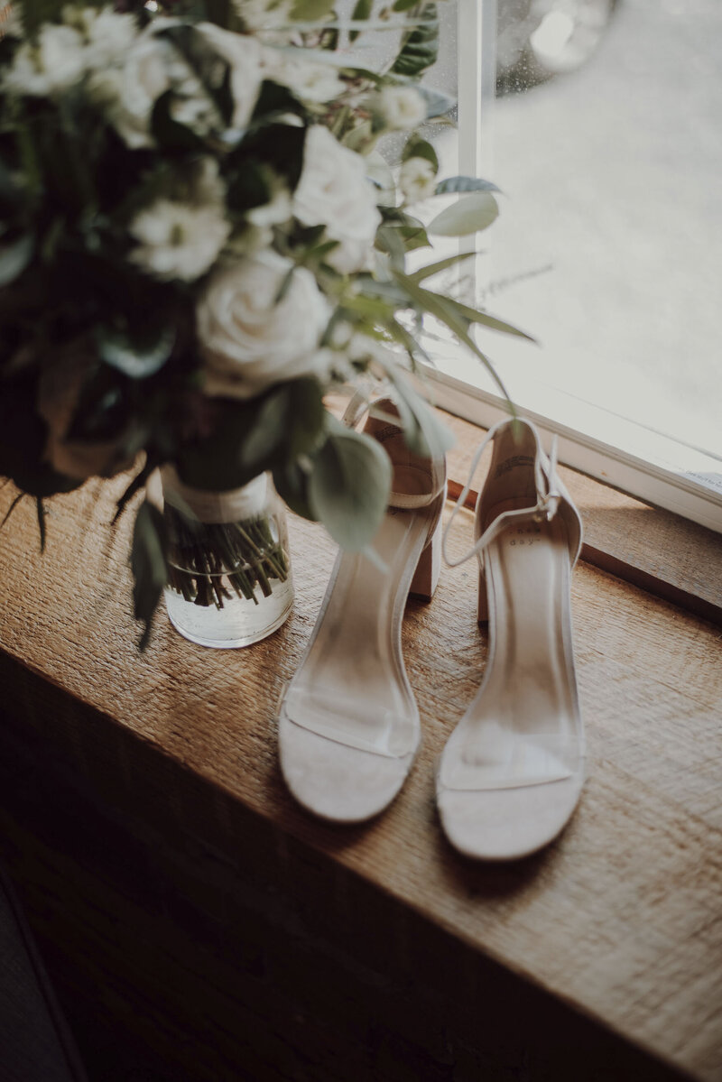 bouquet de mariage et chaussures de mariées devant une fenêtre