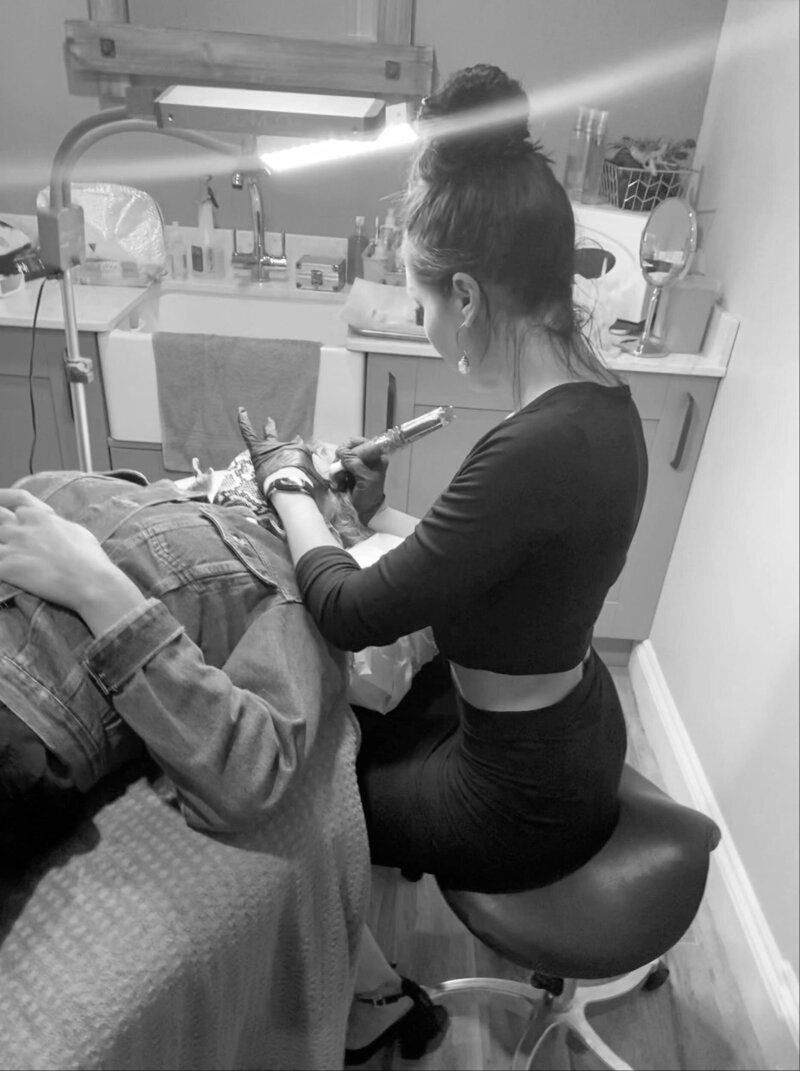 Brittany Smith tattooing a client in salon wearing all black and high bun