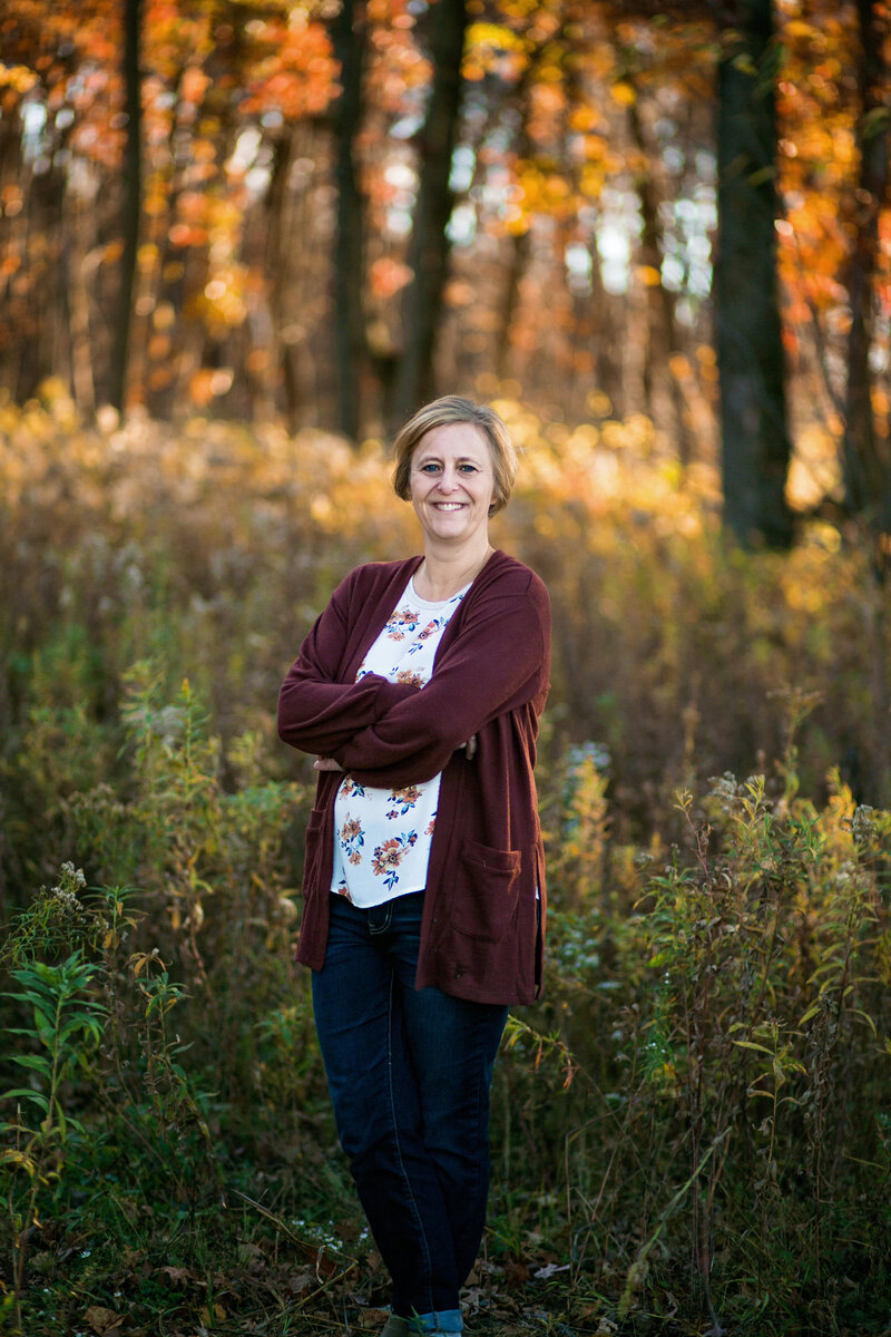 Woman with her arms crossed standing in a field on a sunny fall day.