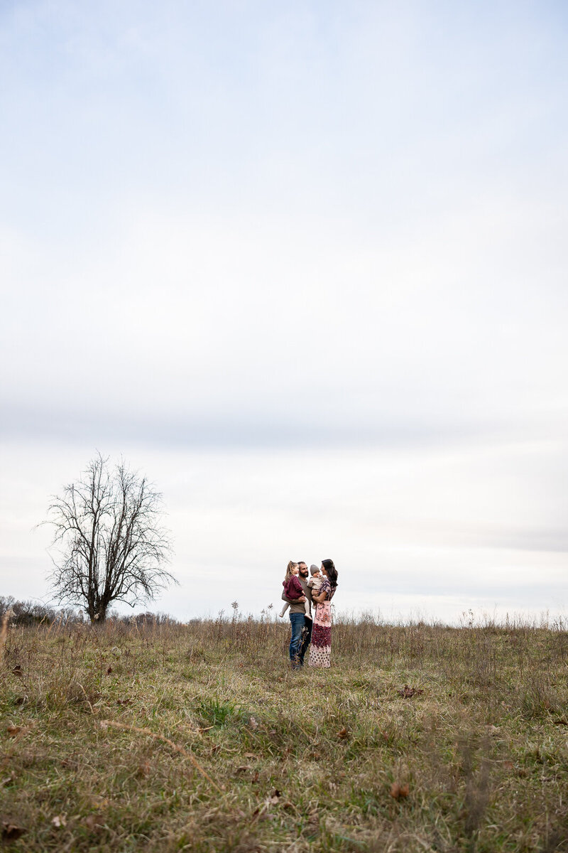 Family portrait of family standing in a field with the sky taking up most of the portrait in De Soto, Missouri. 