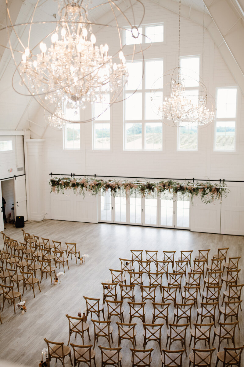 Expansive white barn wedding venue with crystal chandeliers set up for wedding ceremony