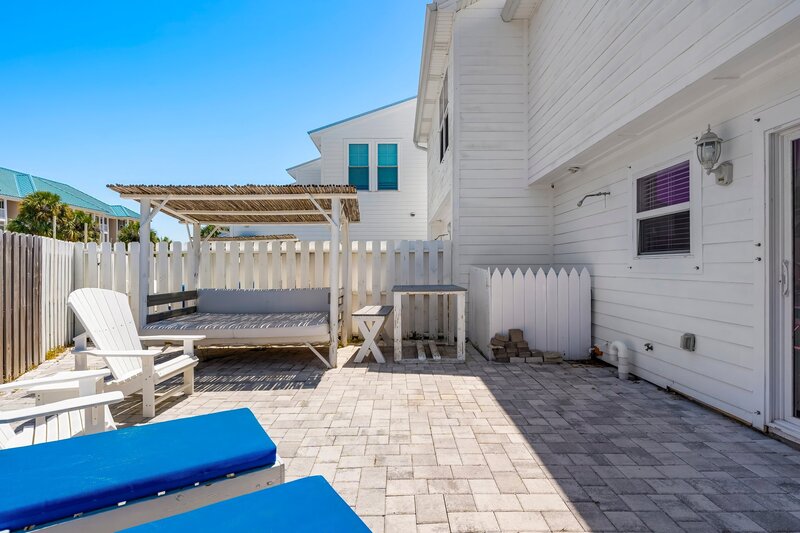 Backyard patio at the Surf House featuring shaded cabana, blue lounge chairs, and white privacy fence for total tranquility.