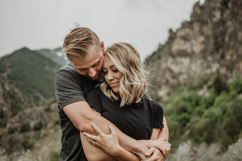 jackson hole photographers captures engagement photos with man standing behind woman and holdin gher from around her shoulders as he leans down and whispers to her for their grand teton photos