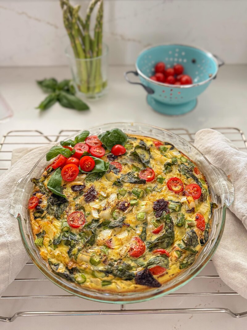Asparagus frittata topped with fresh basil and grape tomatoes.
