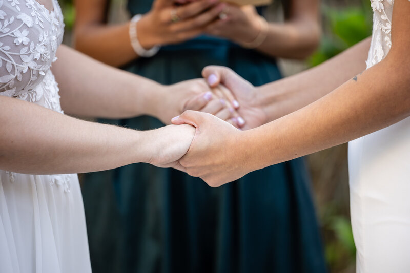 close up of hands of two lesbian brides holding hands while their officiant reads the ceremony script