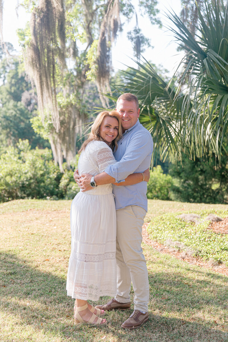 A married couple hug under oak trees during their extended family session for Palmetto Bluff Photographer Lamp and Light Photography.