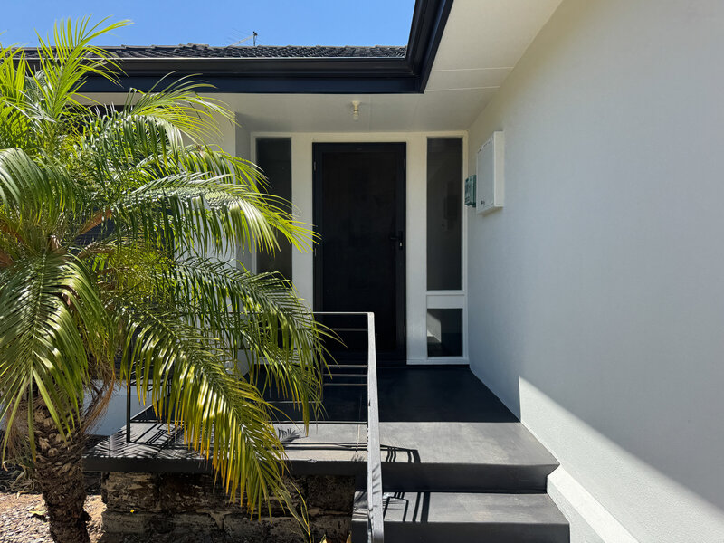 Front exterior entrance of rental property with dark grey steps and fascia and light grey walls. 