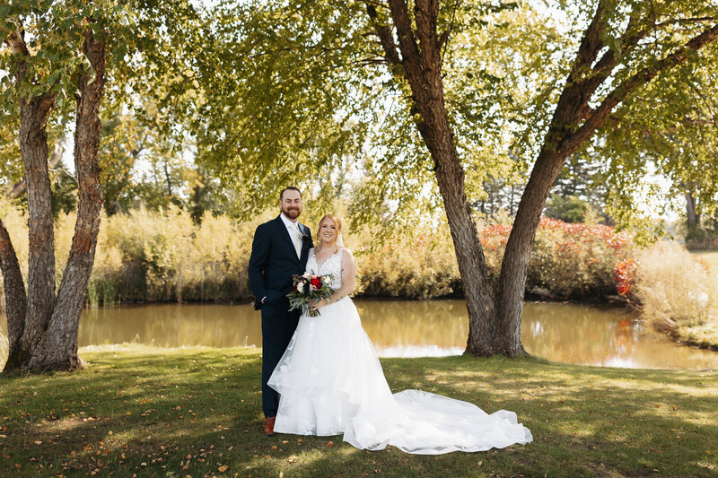 Bride and Groom standing together with bouquet between them smiling